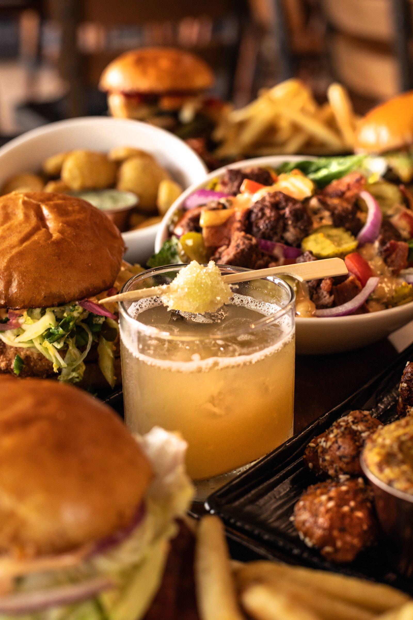 A Ground Rules spread — smashburgers, wings, loaded salad, fries and a hand-shaken cocktail.